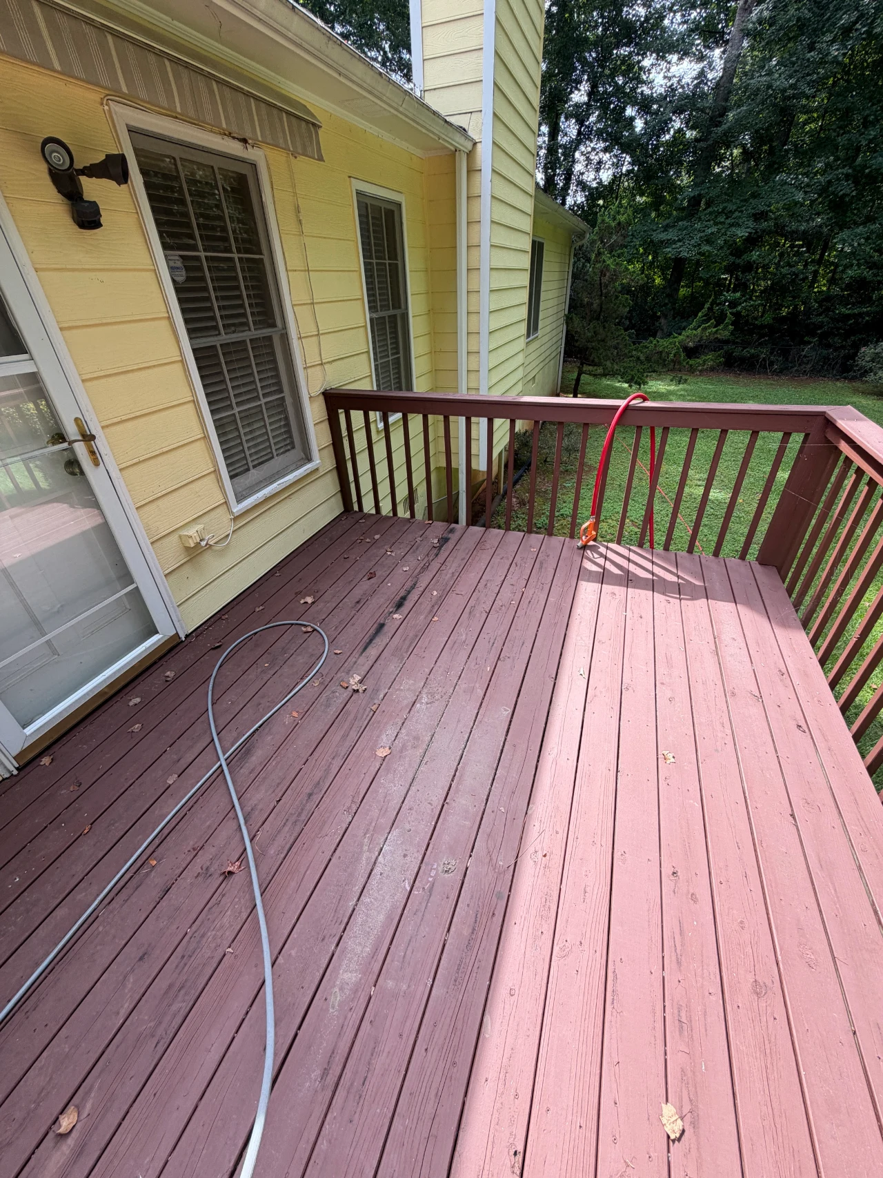 Before photo of a painted wood deck with railing beside a yellow-sided home.