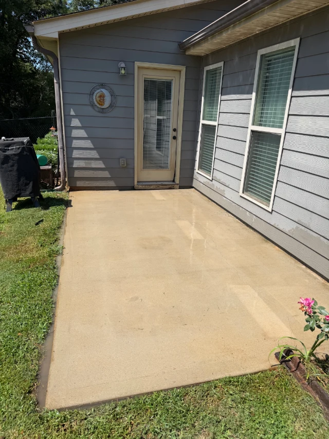Clean concrete patio beside a gray house after pressure washing