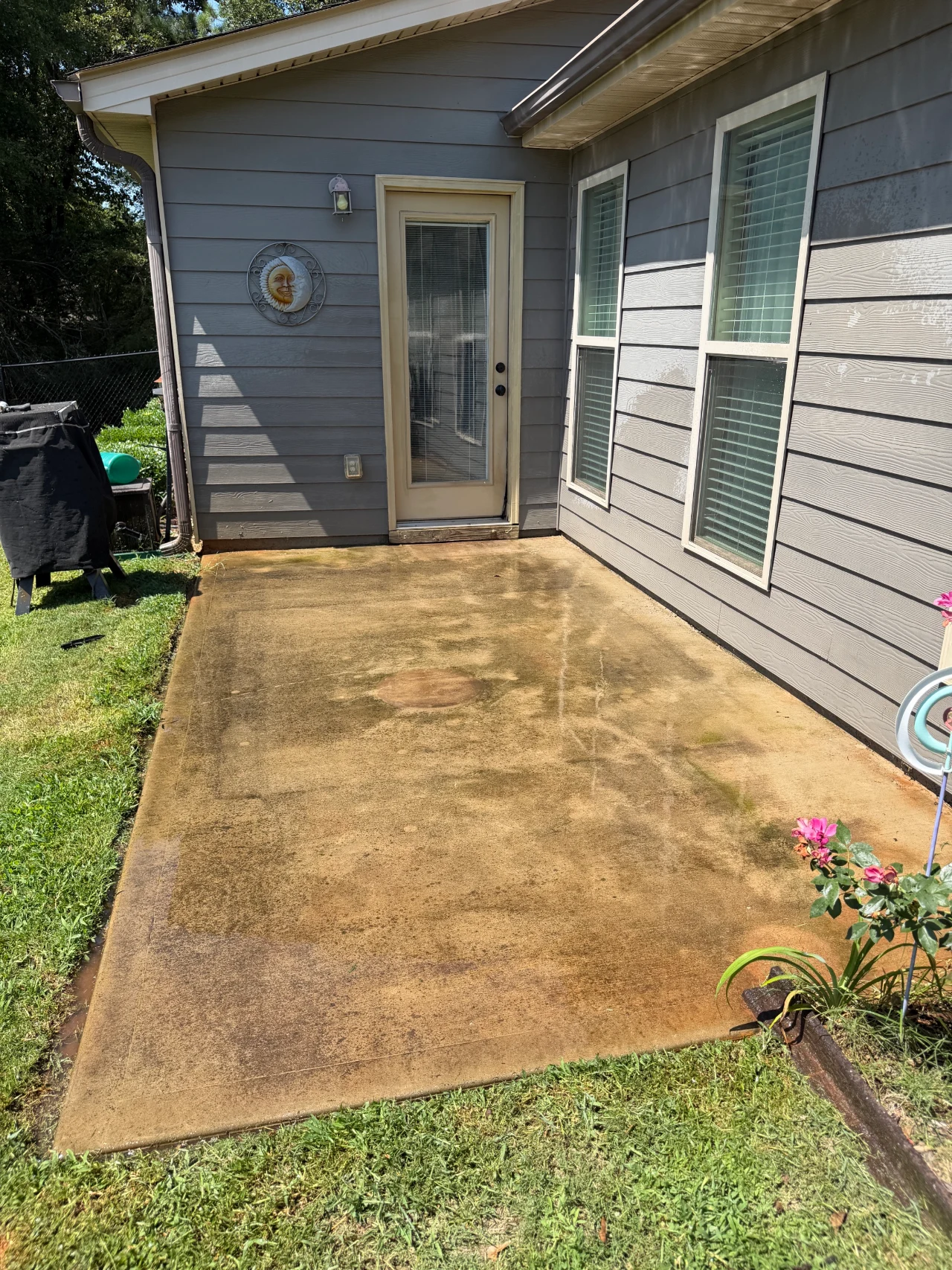 Stained concrete patio beside a gray house before pressure washing